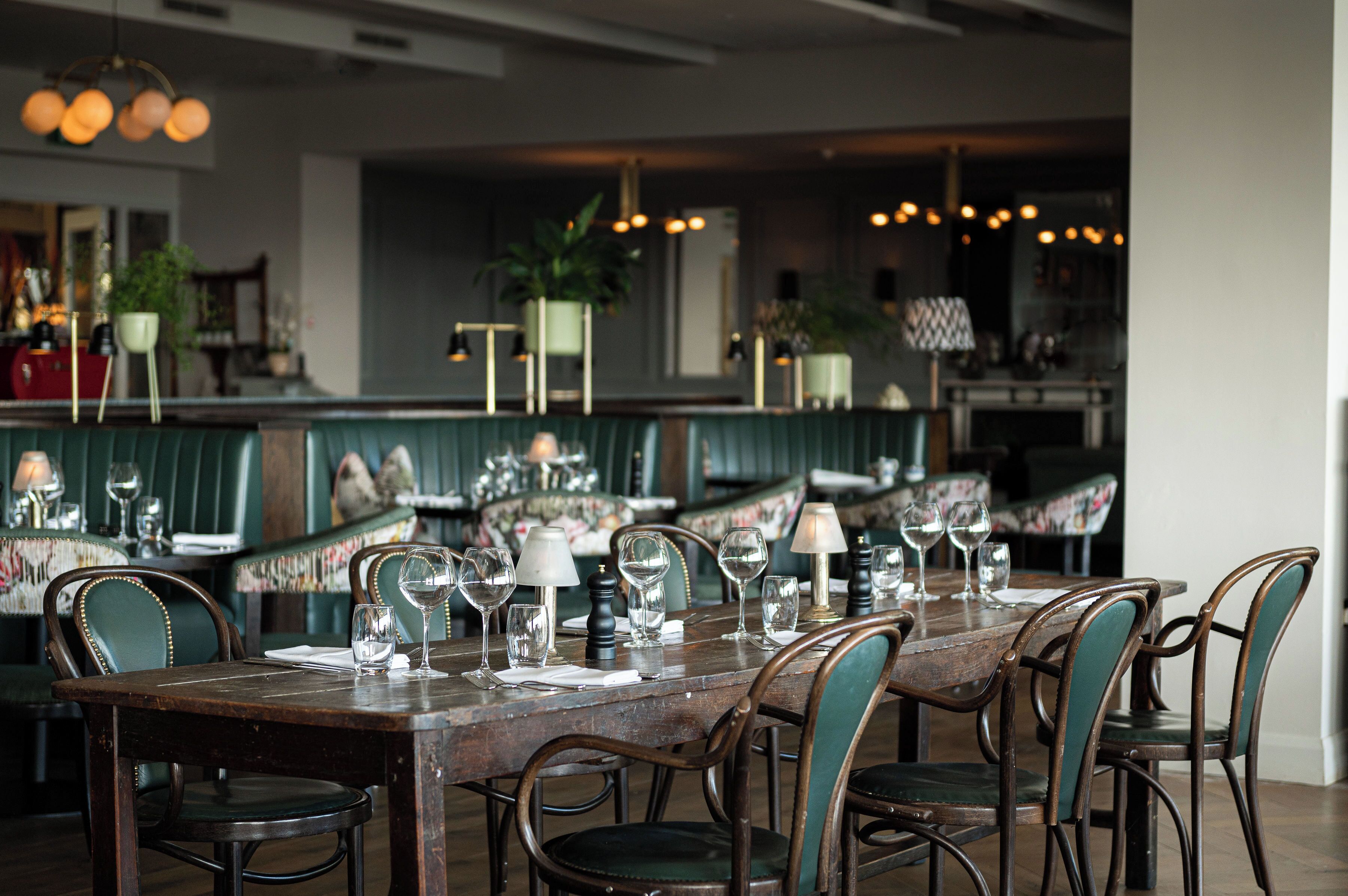 Un restaurante con una larga mesa de madera dispuesta para comer, rodeada de sillas tapizadas.