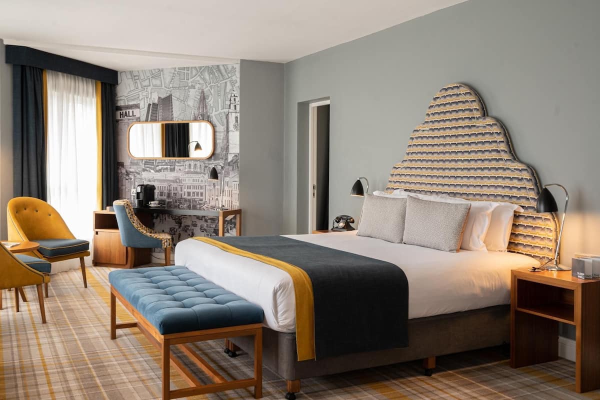 Ein Hotelzimmer mit Bett, Schreibtisch, Stuhl, Bank, Spiegel und einer Wand mit Stadtbild-Motiv.