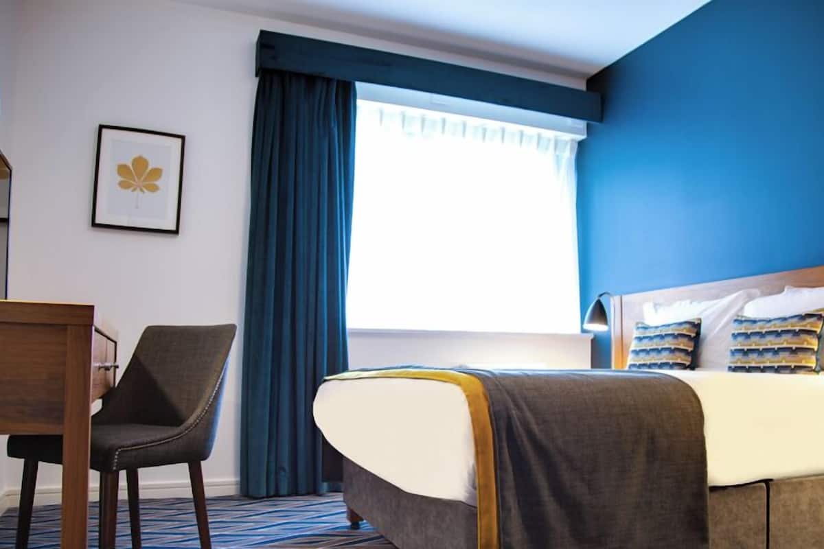 Ein Hotelzimmer mit einem Bett, einem Schreibtisch, einem Stuhl und einem Fenster mit Vorhängen.