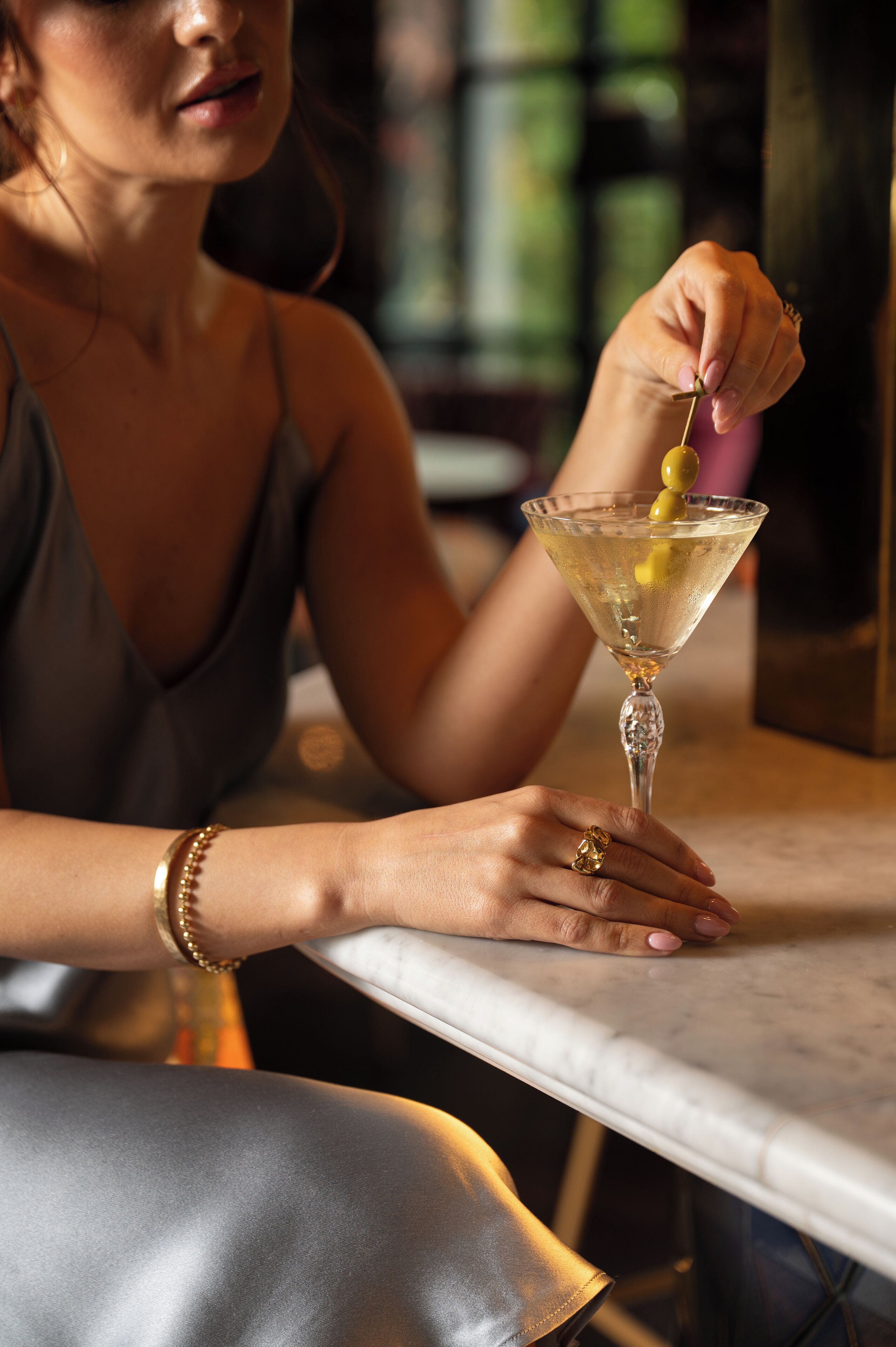 A person holding a martini glass with an olive garnish.