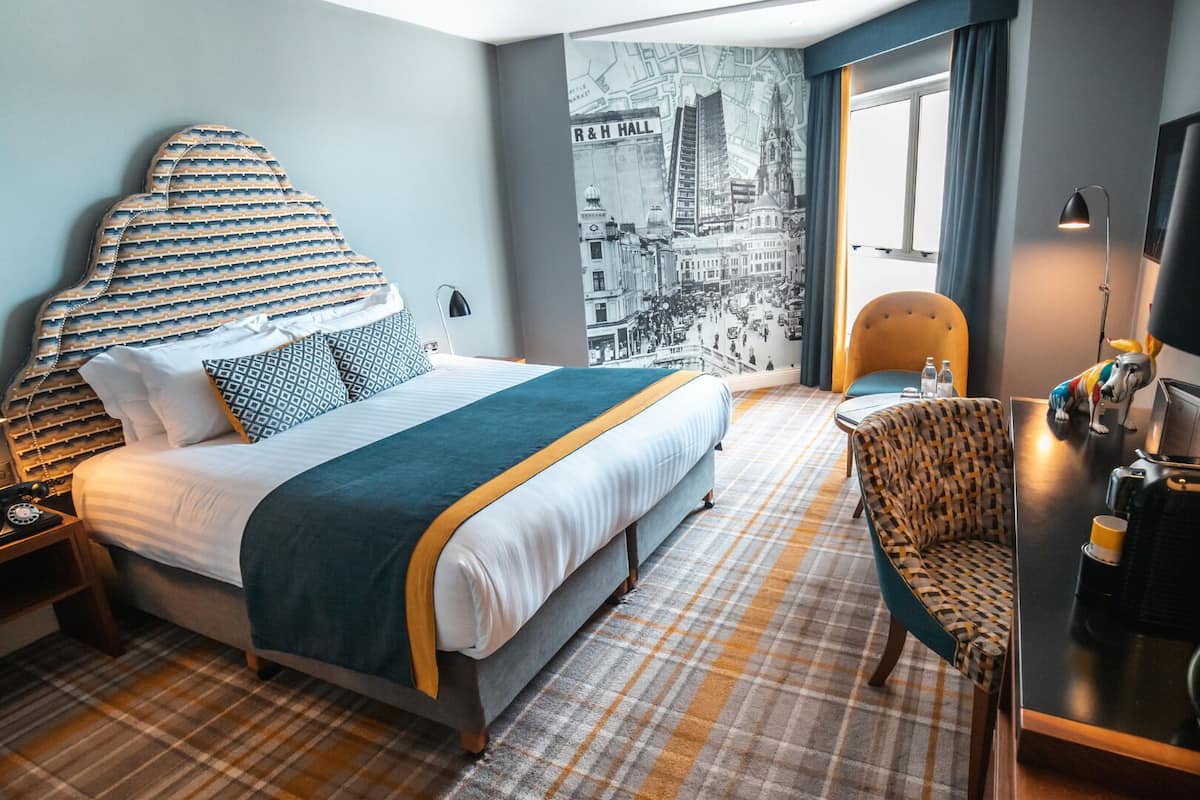 Ein Hotelzimmer mit Bett, Stuhl, Schreibtisch, Lampe und Spiegel.