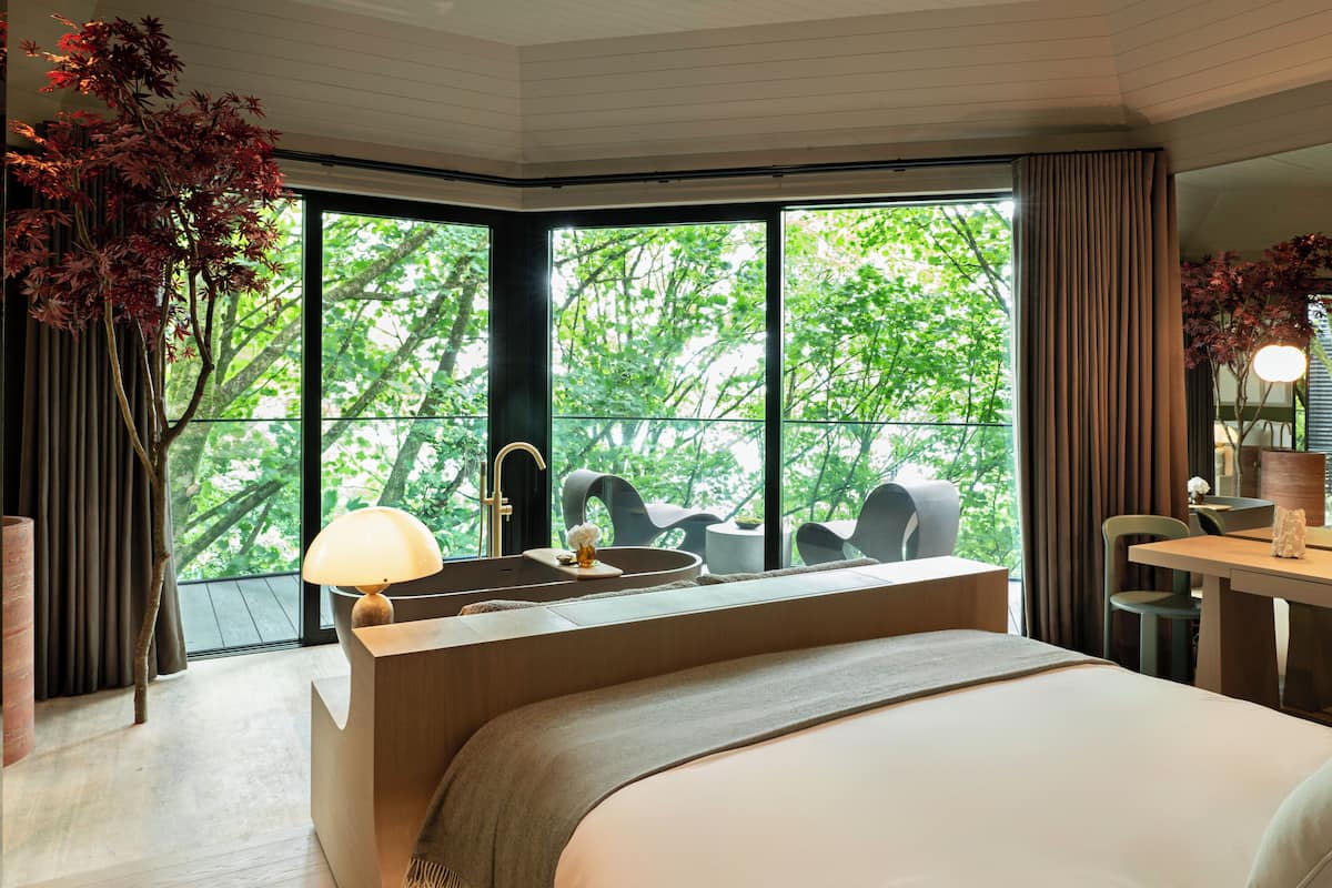Ein modernes Hotelzimmer mit großem Fenster, einem Bett, einem Schreibtisch und einem Sessel.