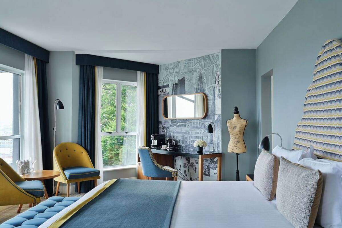 Ein Hotelzimmer mit einem Bett, einem Schreibtisch mit Stuhl, einer Mannequin und einem großen Fenster.