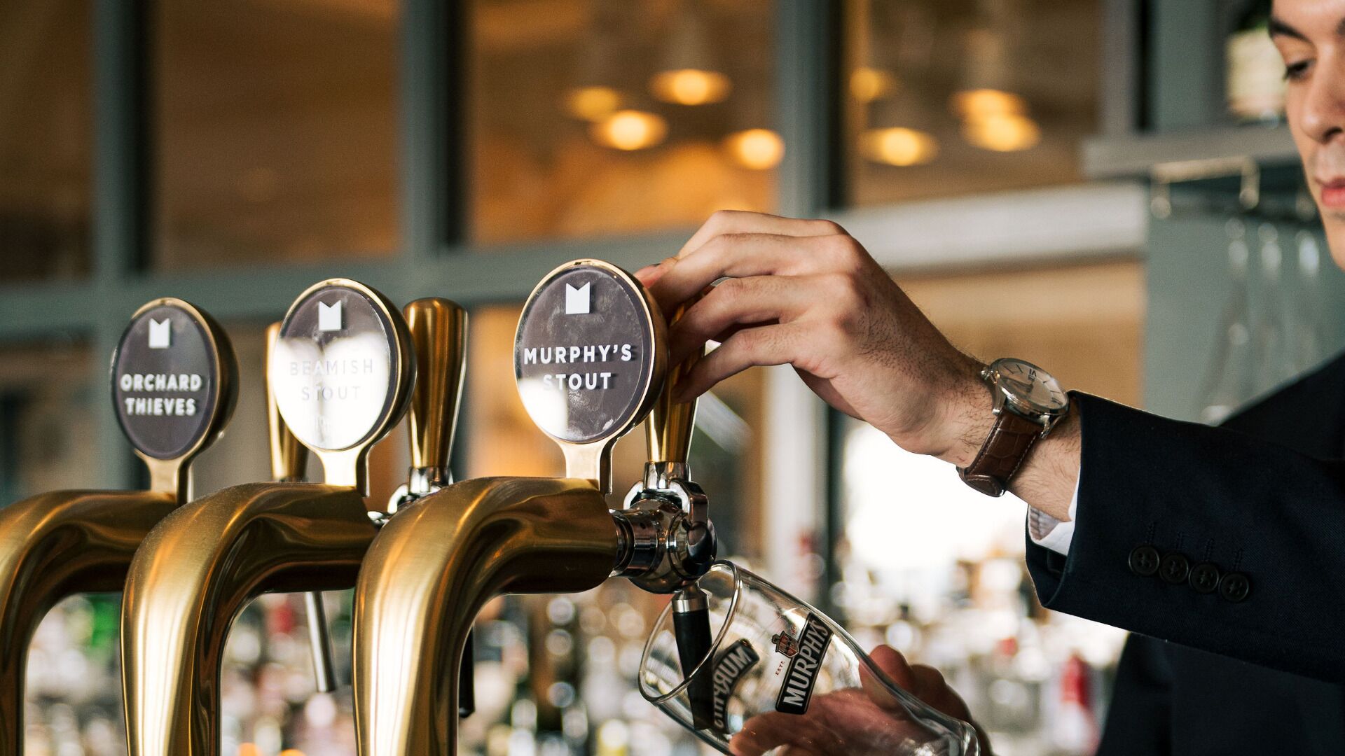 Un cantinero sirviendo una bebida de una grifo con la etiqueta "MURPHY'S STOUT" en un vaso.