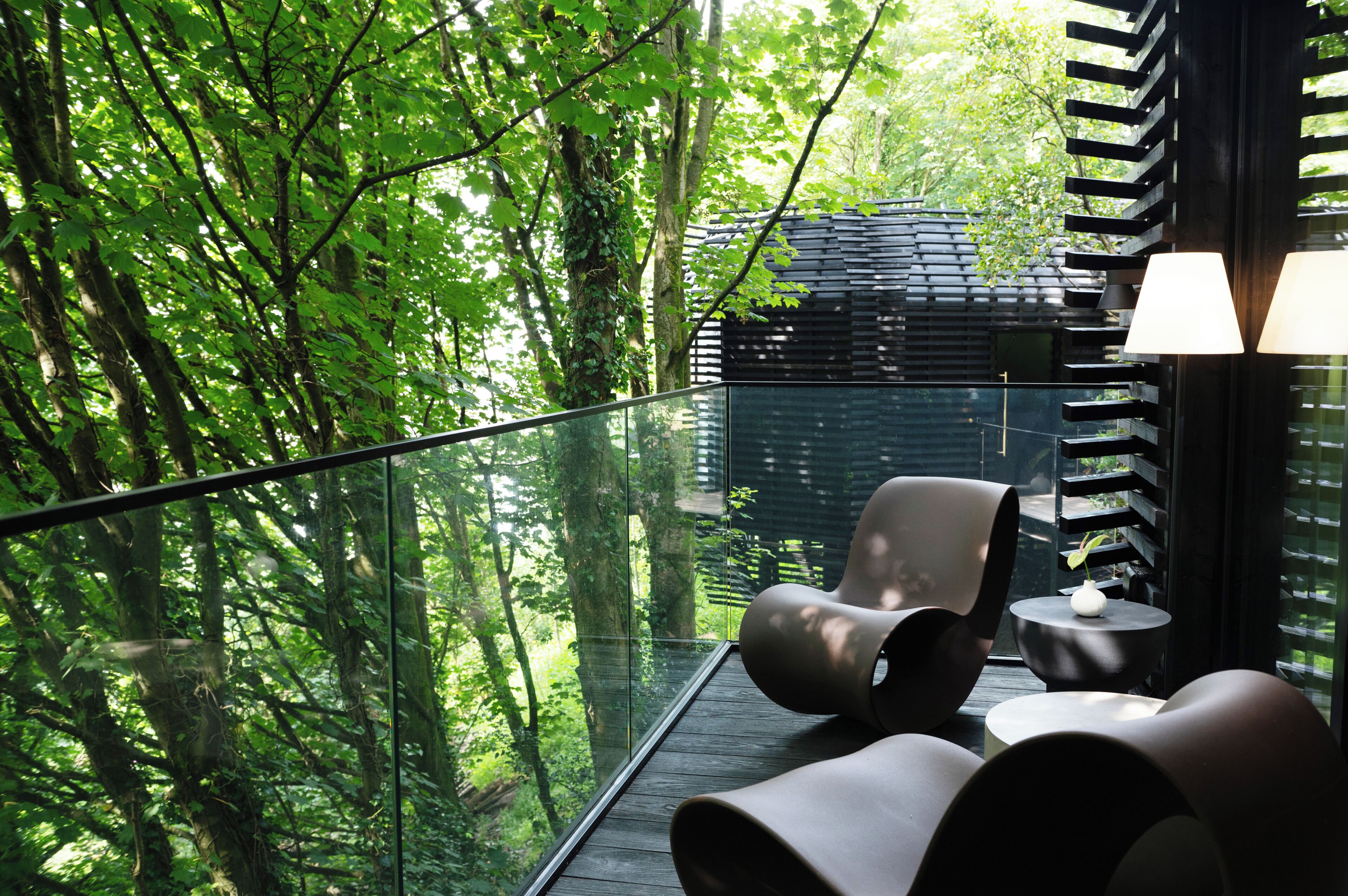 A modern outdoor seating area with a glass balustrade overlooking a forested area.