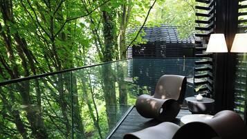A modern outdoor seating area with a glass balustrade overlooking a forested area.