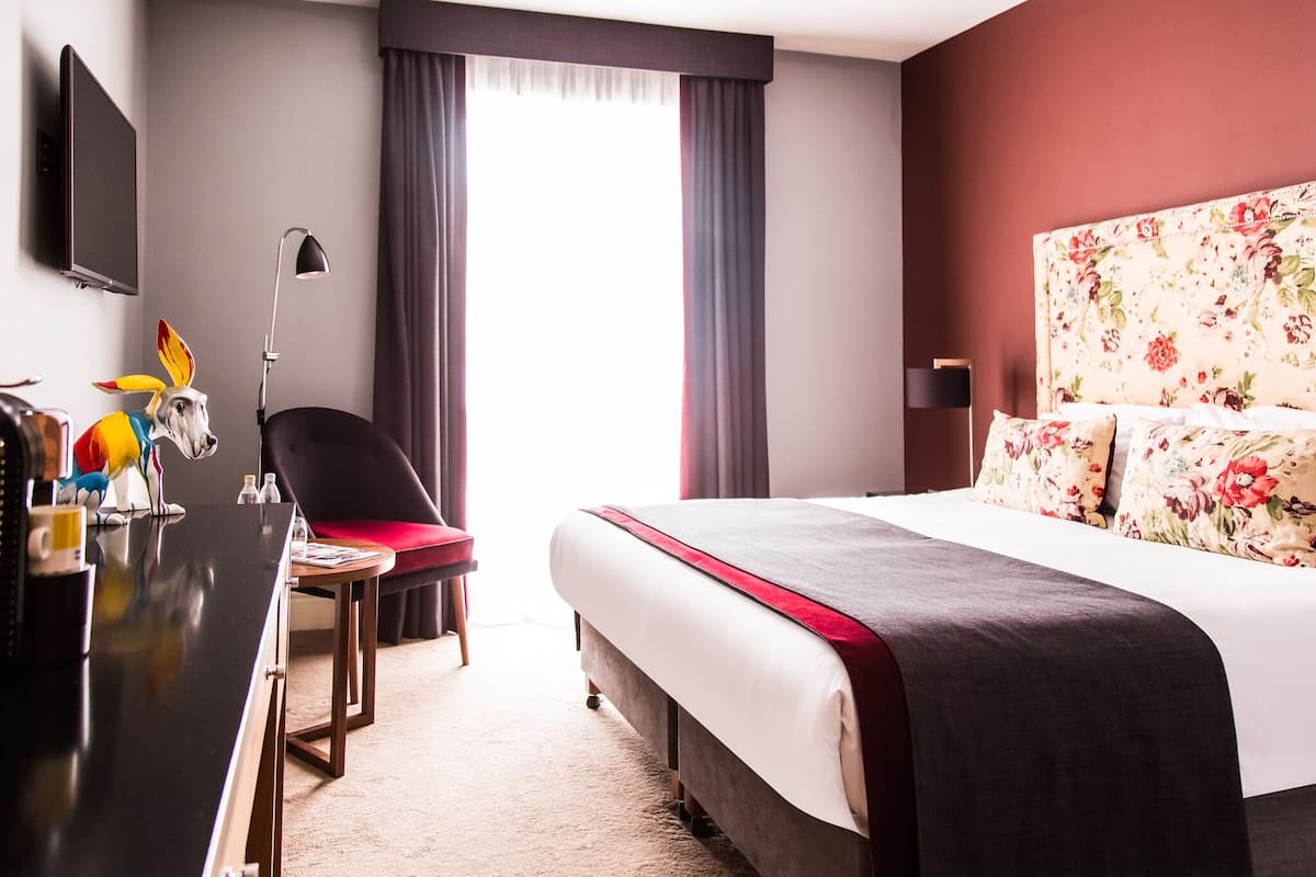 Ein Hotelzimmer mit Bett, Schreibtisch, Stuhl, Fernseher und einem fensterbepflanzten Fenster.
