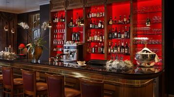 A bar area with a long counter, multiple shelves of bottles, and bar stools.