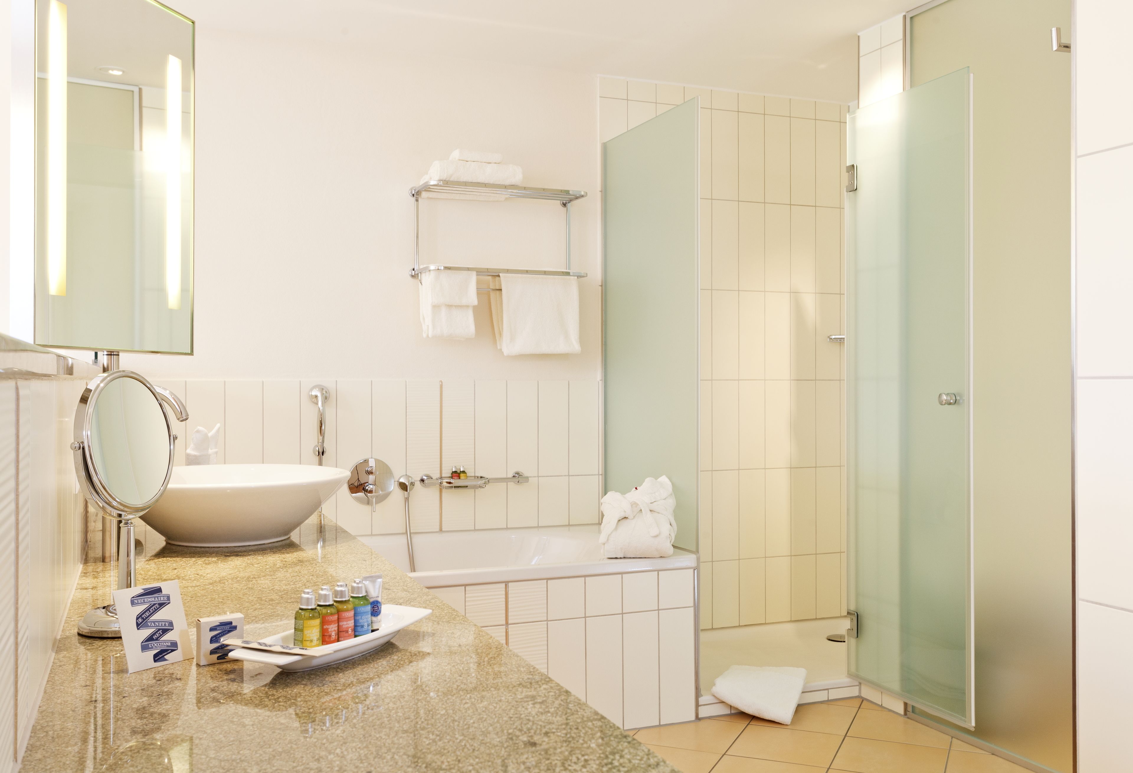 A modern bathroom with a freestanding bathtub, a large mirror, a vanity with toiletries, and a glass shower enclosure.