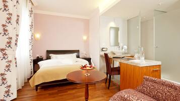 Una habitación de hotel con una cama, una mesita redonda con un frutero, un escritorio con espejo y una silla.