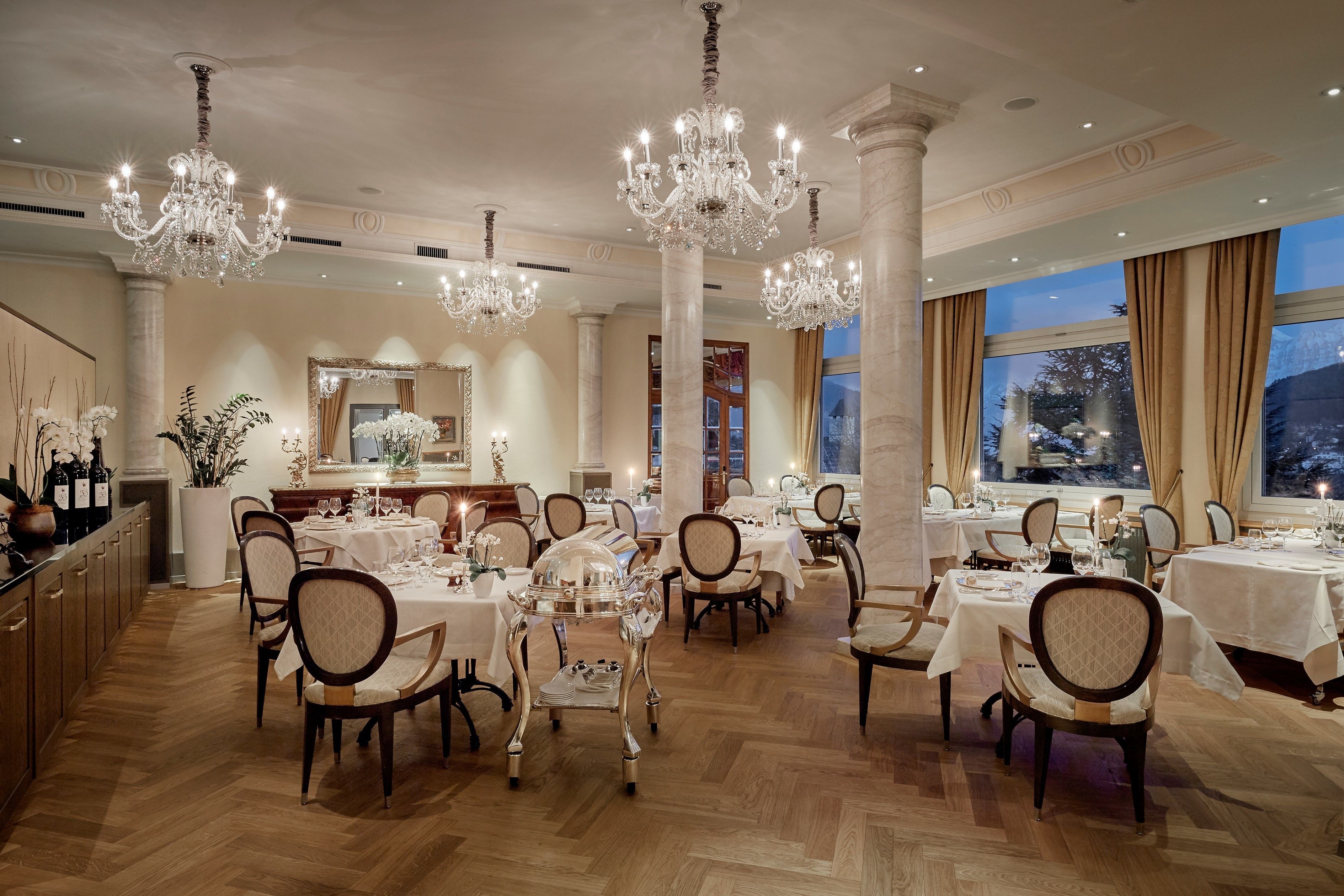 A formal dining room with chandeliers, tables set for multiple guests, and a large mirror.
