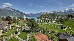 A residential area with houses, a tennis court, and a lake with mountains in the background.