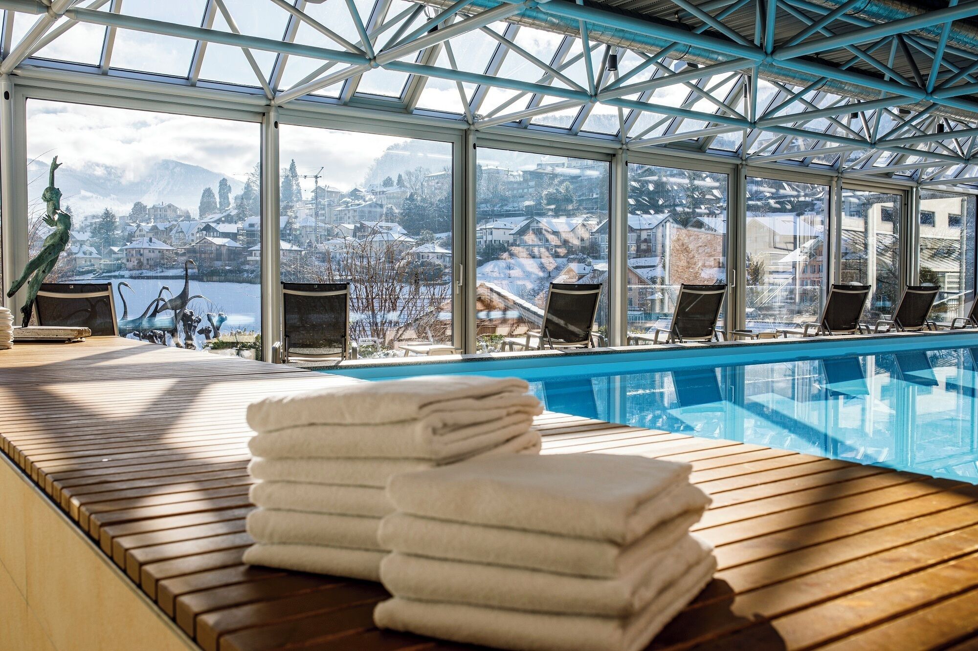 An indoor swimming pool with a view of a snowy landscape and a city in the background.