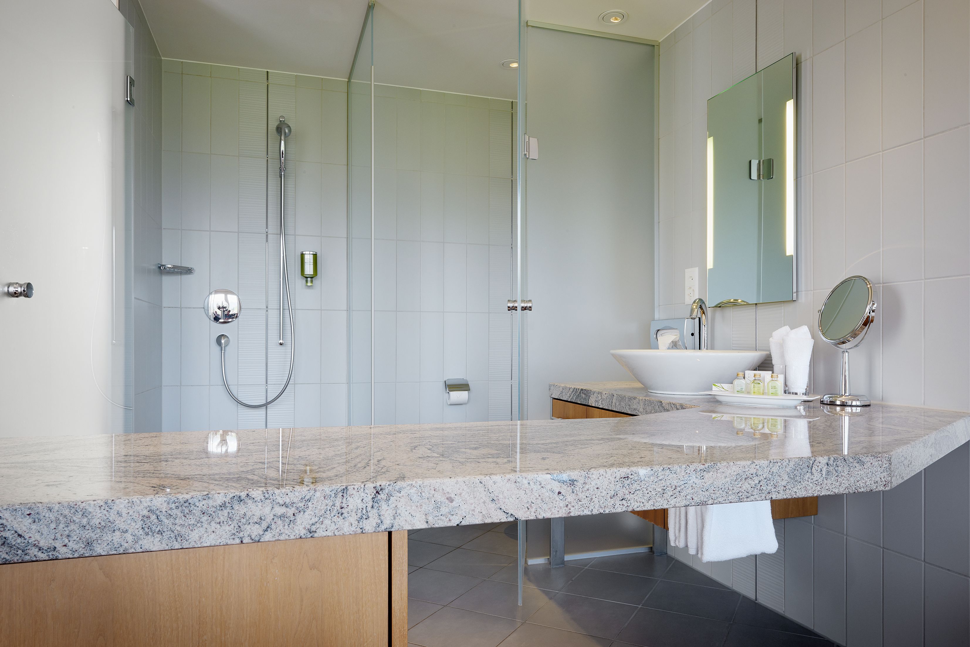 Un baño moderno con una amplia encimera de mármol, una bañera independiente, ducha con cerramiento de vidrio y un espejo grande.