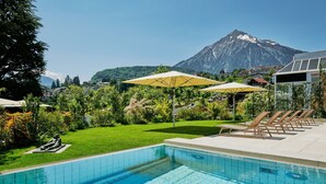 A swimming pool with a view of a mountain, surrounded by greenery and lounge chairs.