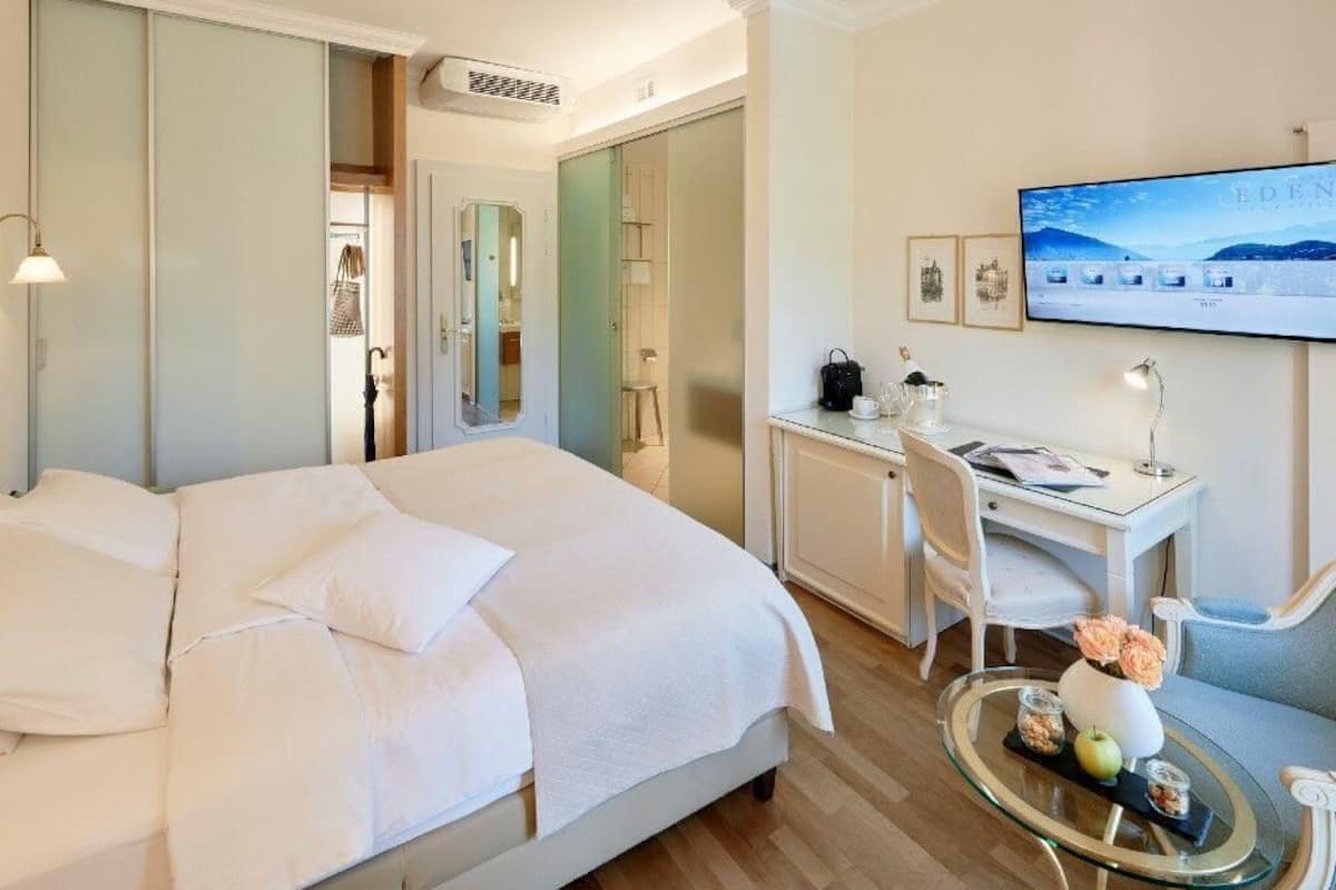 A hotel room with a bed, a desk with a chair, a television, and a small table with decorative items.