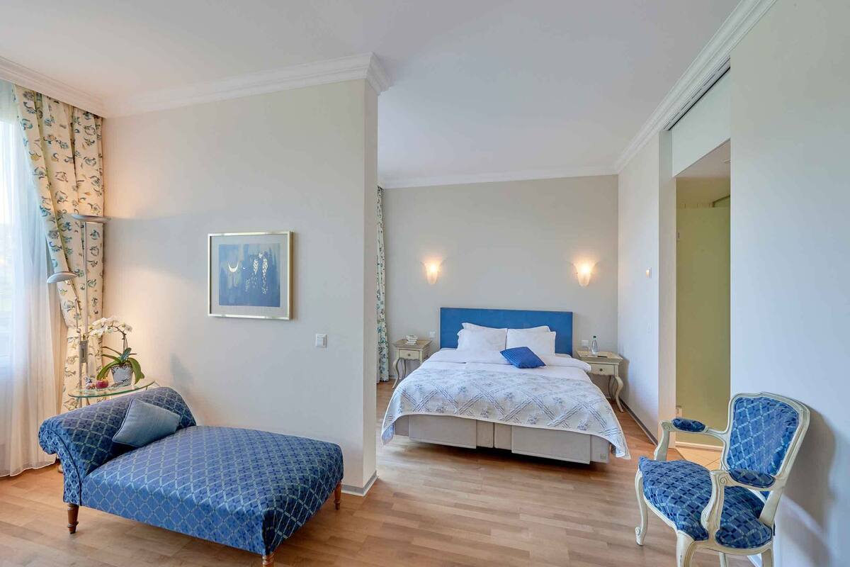 A bedroom with a bed, a chair, a small table, and a potted plant.