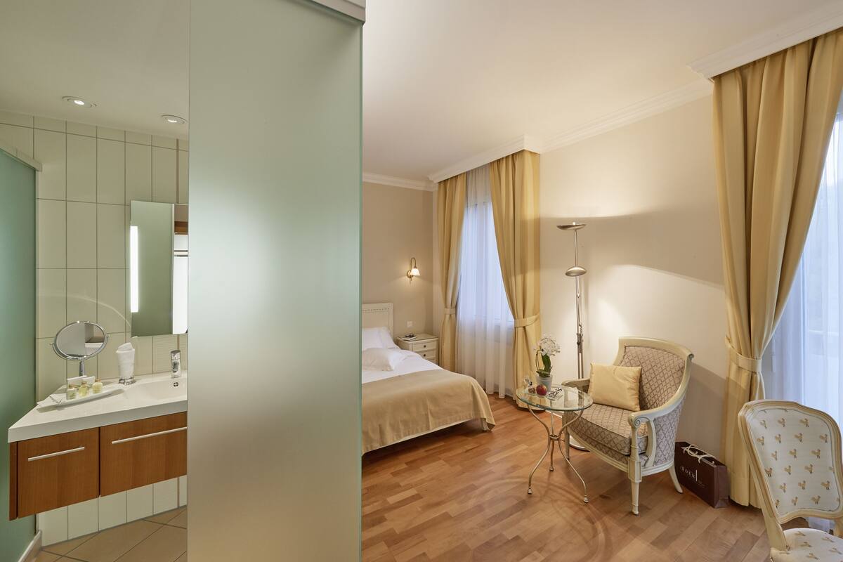 A hotel room with a bed, bedside table, lamp, chair, and a small table with a vase of flowers.