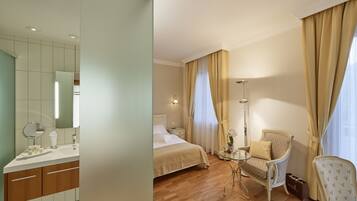 Ein Hotelzimmer mit Bett, Nachttisch, Lampe, Stuhl und einem kleinen Tisch mit Blumenvase.