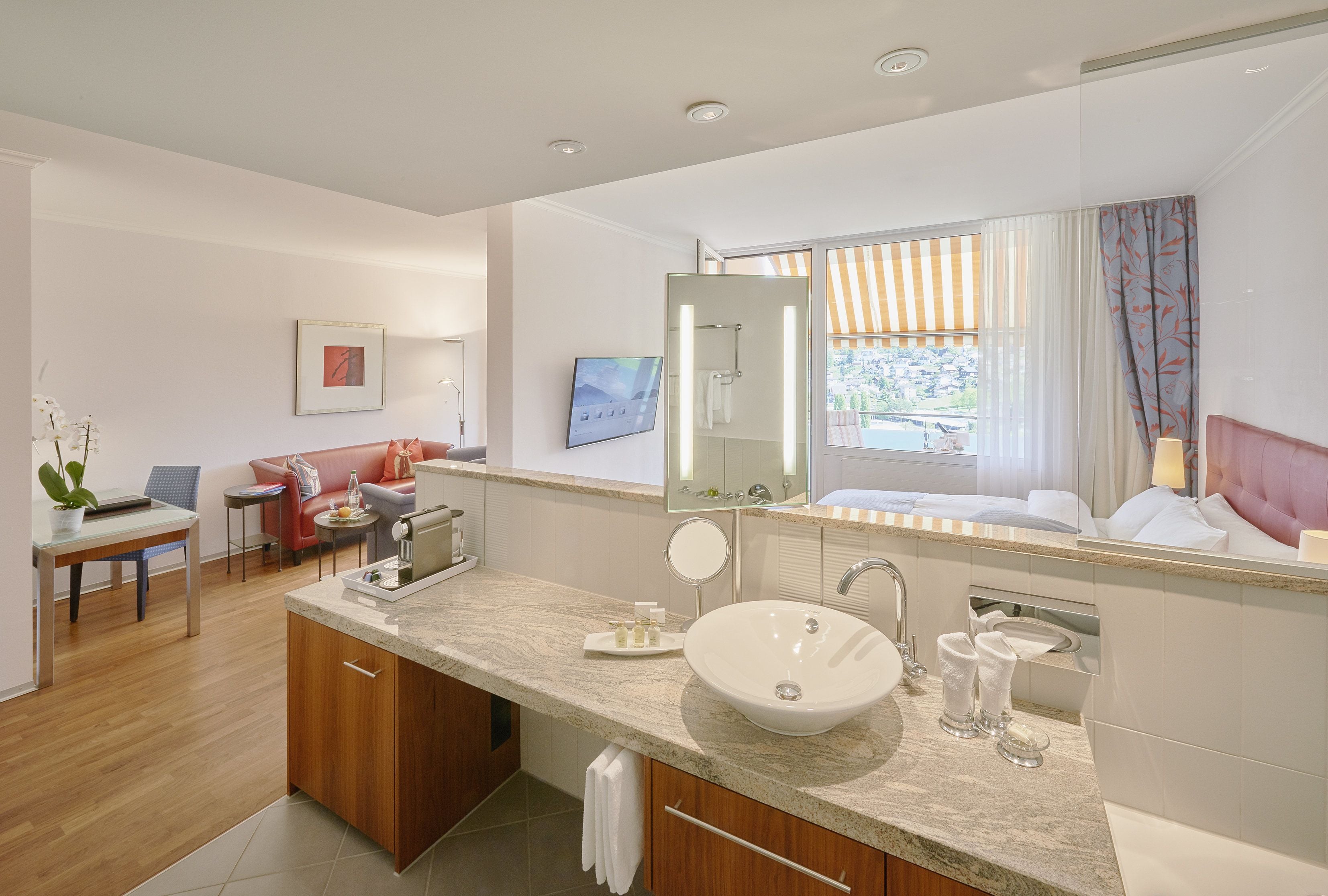 Un baño moderno con un lavamanos grande, un espejo y una ducha. Hay una zona de comedor con una mesa y sillas, y un sofá.