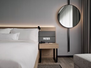 A modern hotel room with a neatly made bed, a bedside table with a lamp, a round mirror, and a power outlet. - AC Hotel by Marriott Penang (George Town)