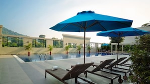 Un espace piscine aménagé sur le toit, avec des chaises longues et des parasols bleus, entouré de plantes en pot et offrant une vue dégagée sur les montagnes.