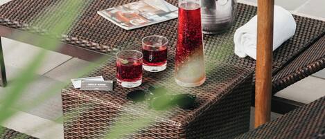 A poolside lounge area with wicker furniture, a metal bucket, and two glasses of red beverage.