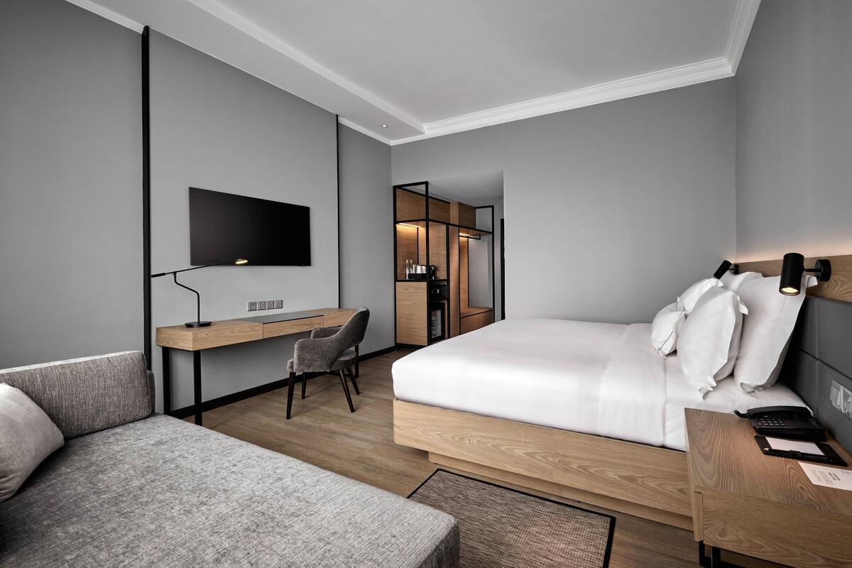 A modern hotel room with a large bed, a desk, a chair, and a TV mounted on the wall.
