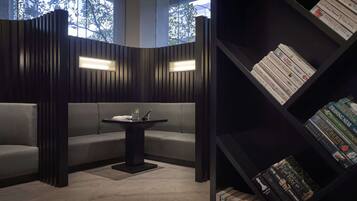 A modern reading area with a dark wood panel wall, a central table with a plant, and a bookshelf filled with books.