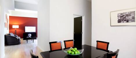 Un coin repas avec une table noire, quatre chaises et un saladier de pommes vertes.
