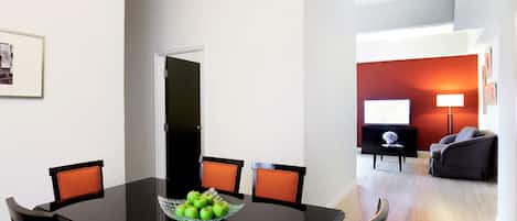 Un comedor con una mesa negra, sillas naranjas y un cuenco de vidrio con manzanas verdes.