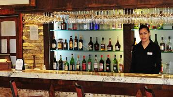 Un espace bar avec un barman, des étagères remplies de bouteilles d’alcool et un mur en pierre en arrière-plan.