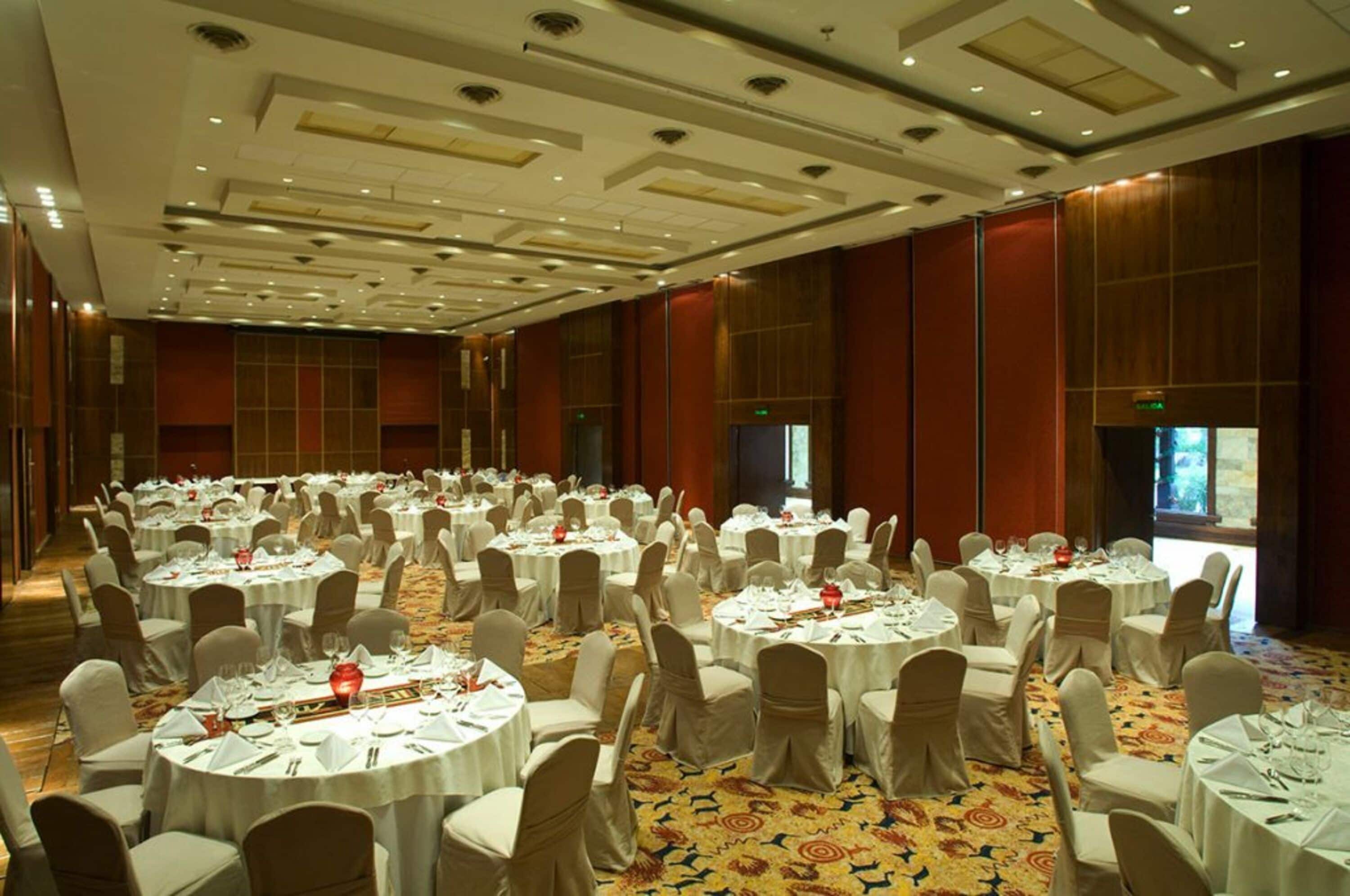 A large banquet hall with round tables set for dining, equipped with white tablecloths and chairs.