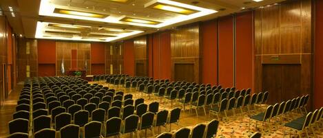 A conference room with rows of chairs, a carpeted floor, and wooden paneling on the walls.