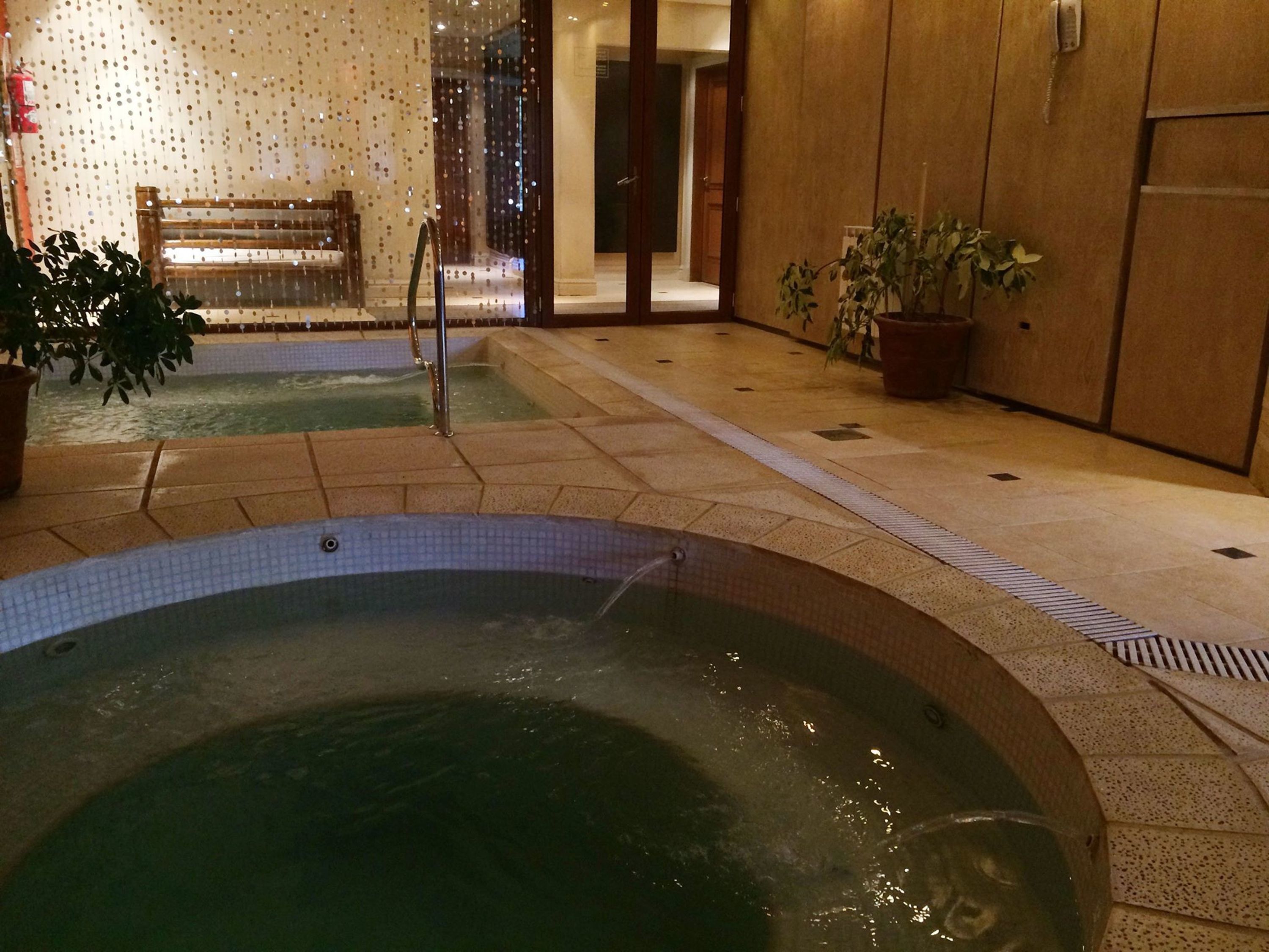 Ein Whirlpoolbereich mit gefliestem Boden, einer Sitzbank und Topfpflanzen.