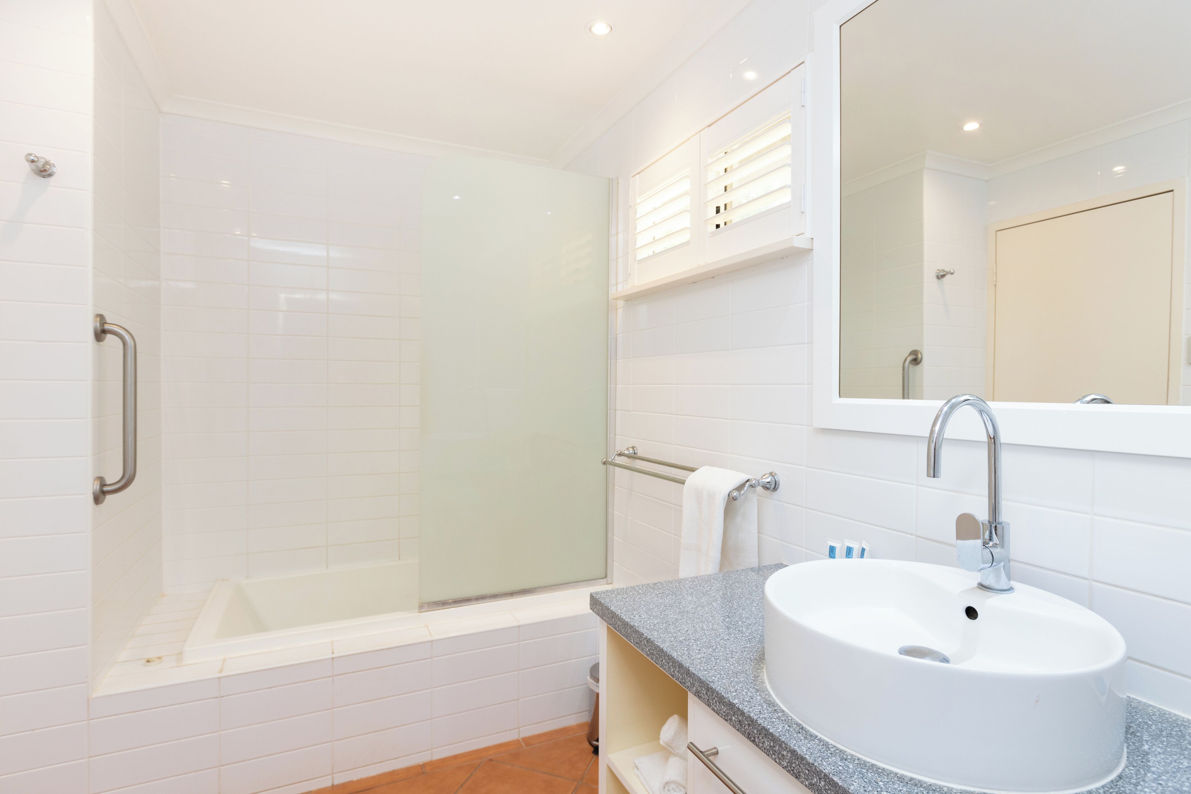 A modern bathroom with a glass-enclosed shower, a white sink, and a large mirror.