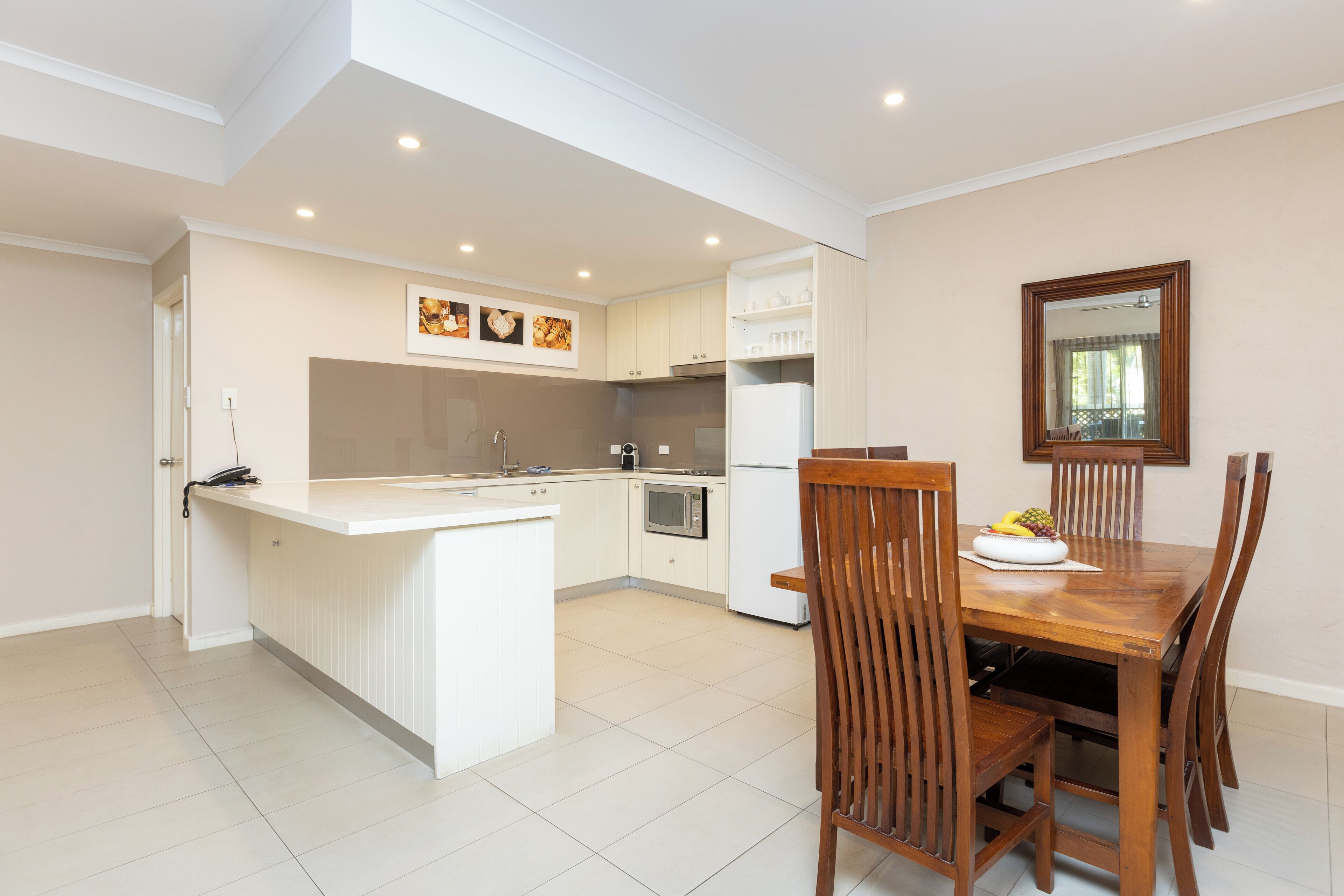 A modern kitchen with white cabinetry, a central island, and a dining area with wooden chairs and a table.
