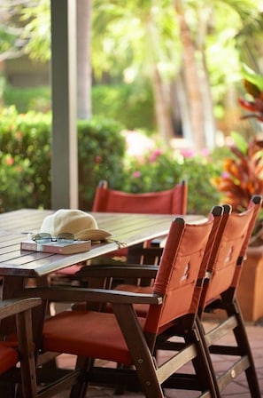 A wooden table with a white hat and glasses on it, surrounded by red chairs.