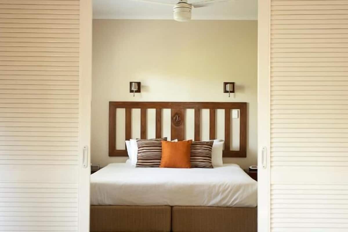 Quarto com cabeceira de madeira, cama com roupa de cama branca, duas luminárias de cabeceira e um ventilador de teto.