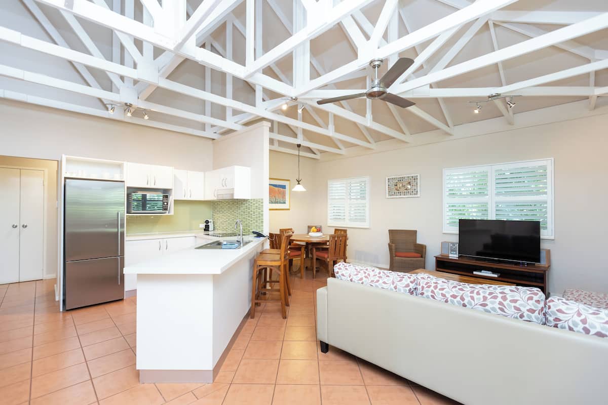 Cozinha espaçosa com ilha central, sala de jantar e sala de estar com sofá e televisão.