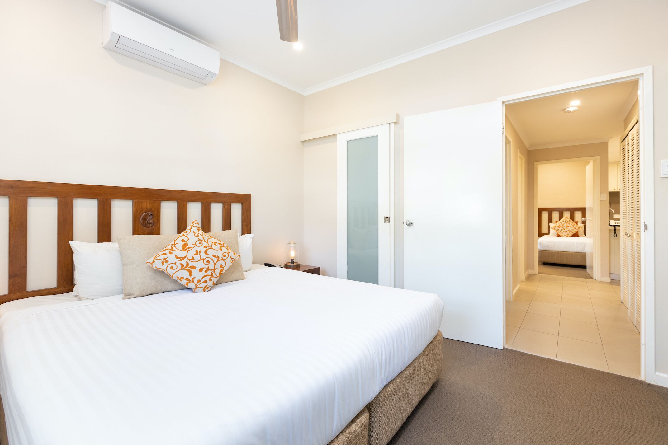 A hotel room with a large bed, a bedside table with a lamp, a wardrobe, and a door leading to a bathroom.