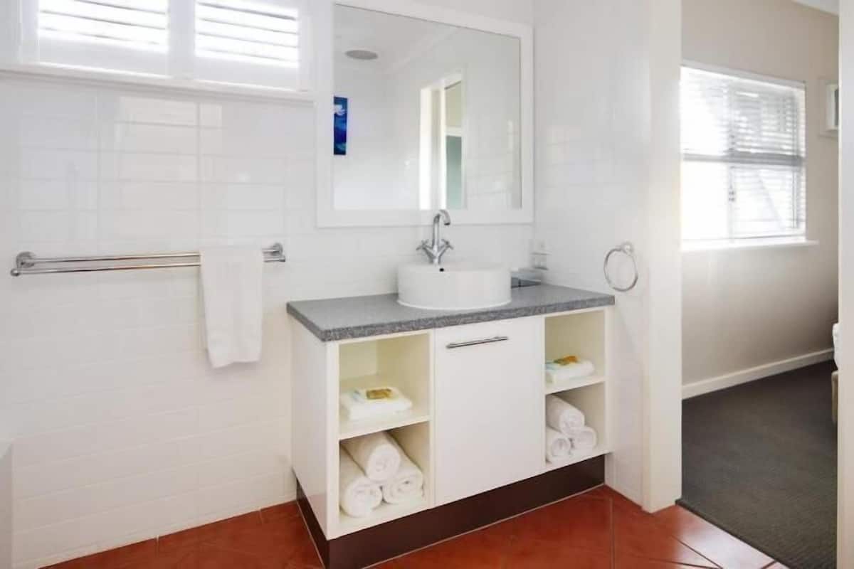 Um banheiro com pia branca, espelho acima, porta-toalhas e vaso sanitário.