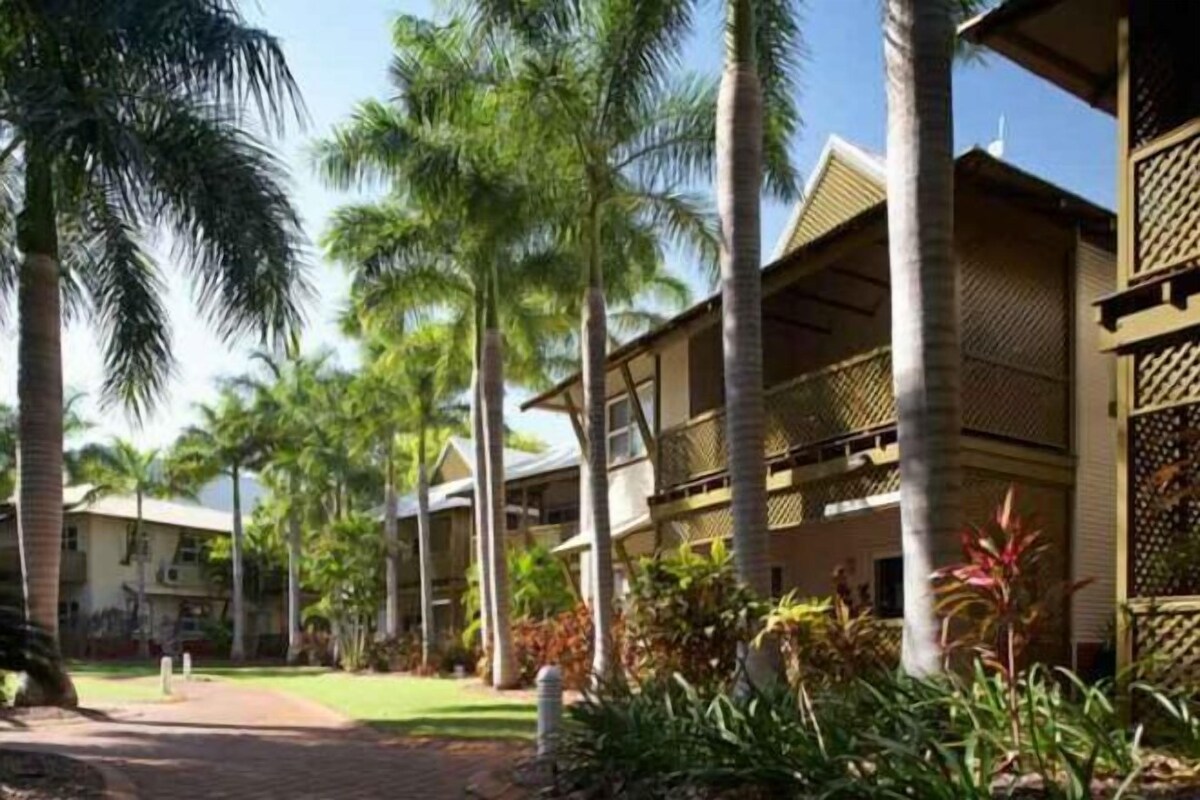 A resort with multiple-story buildings, palm trees, and a paved walkway.