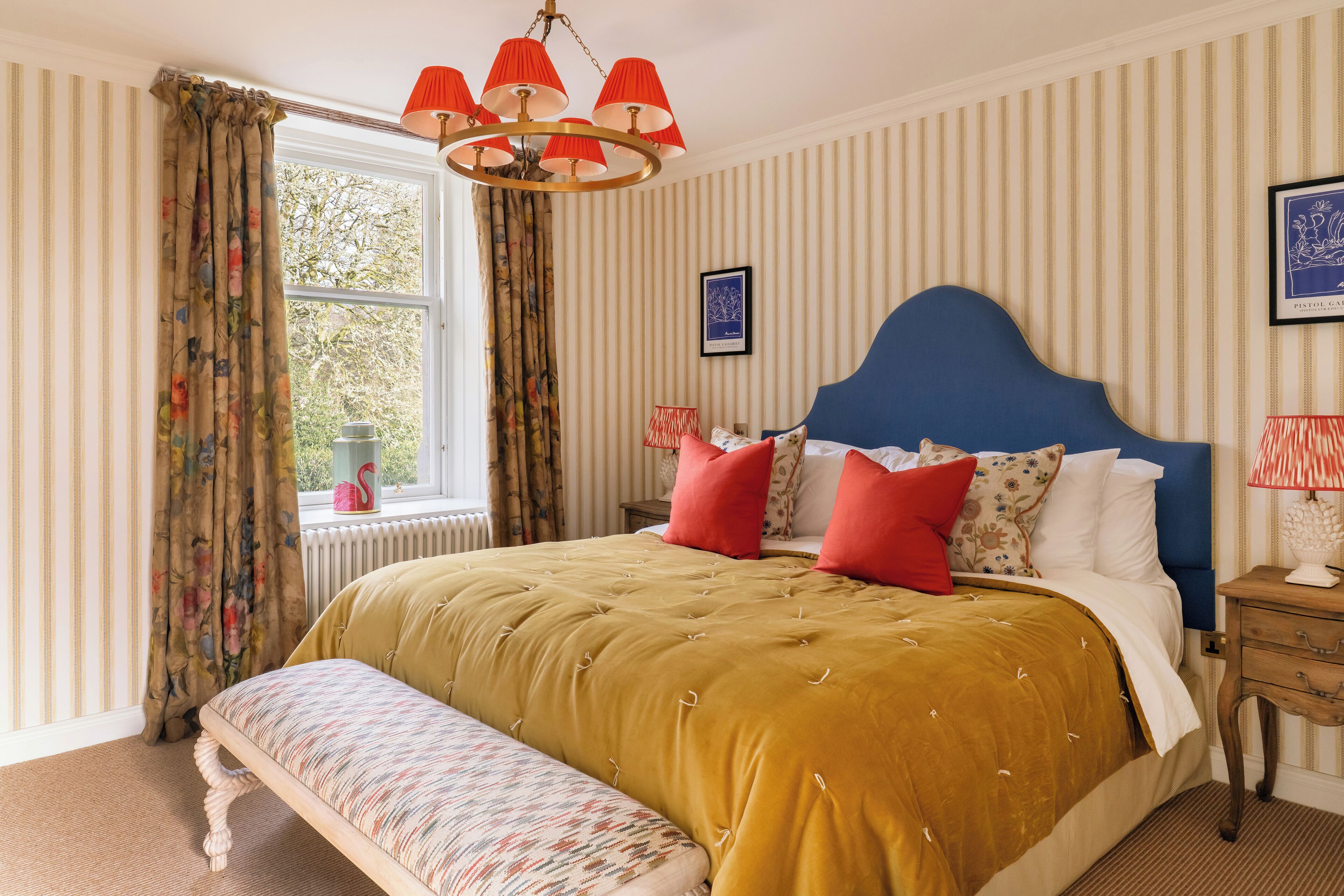 A neatly arranged bedroom with a large bed, a bench, a nightstand, and a window with curtains.