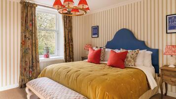 A neatly arranged bedroom with a large bed, a bench, a nightstand, and a window with curtains.