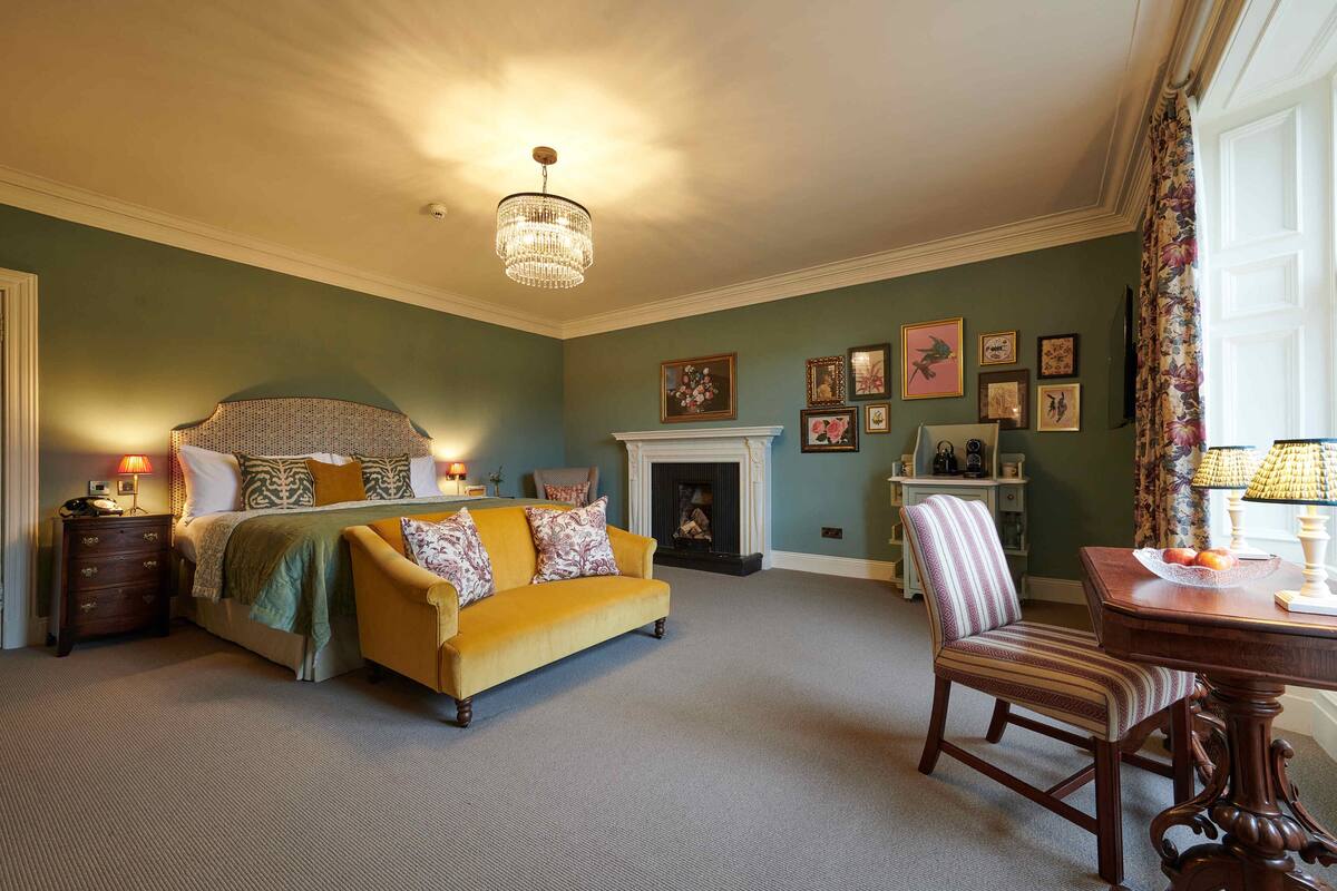 Un dormitorio con cama, sofá amarillo, chimenea y mesa de comedor.