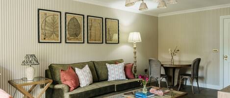 A living room with a sofa, a coffee table, a lamp, and framed botanical prints on the wall.