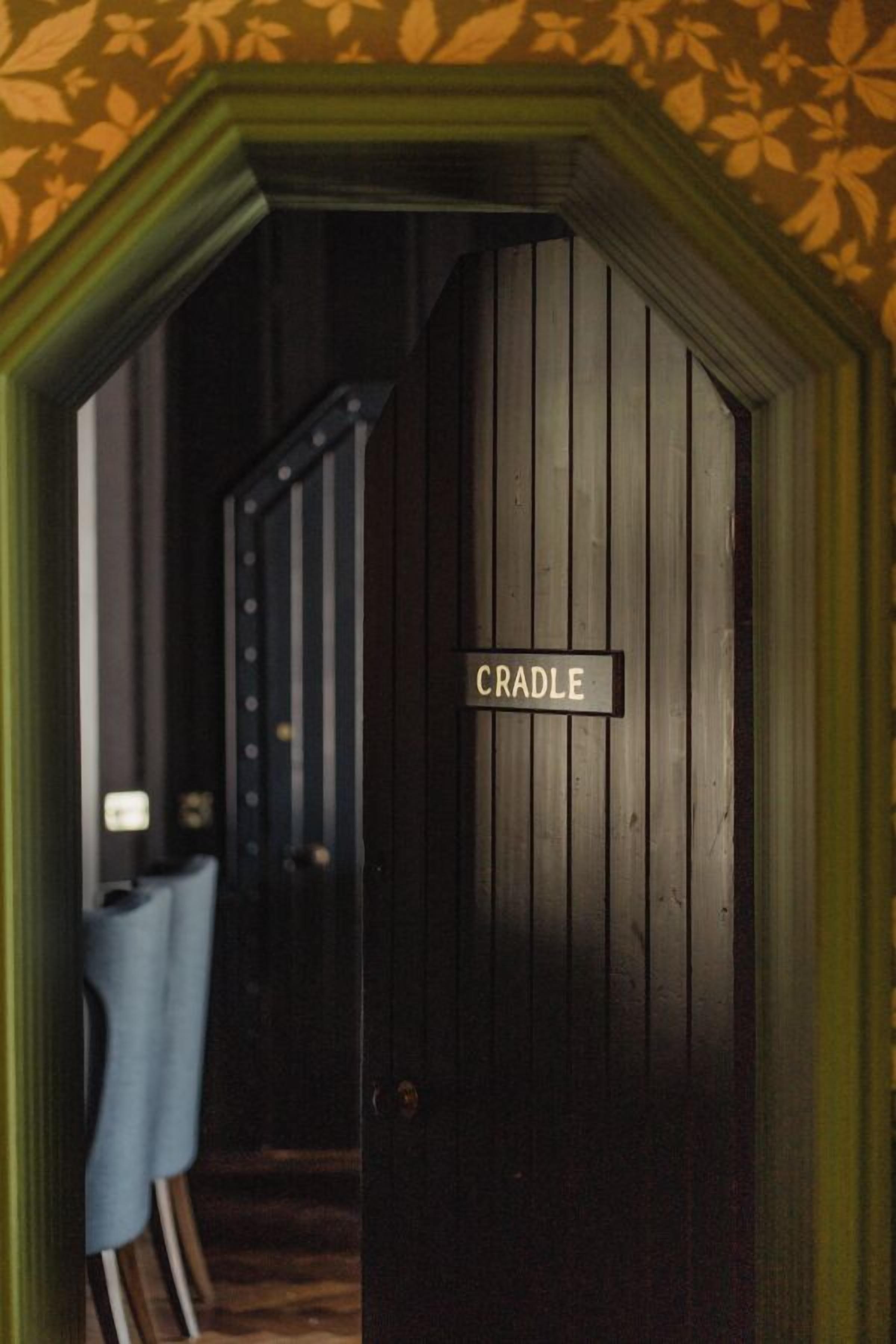 Um quarto com uma porta identificada com 'CRADLE' e uma escada ao fundo.
