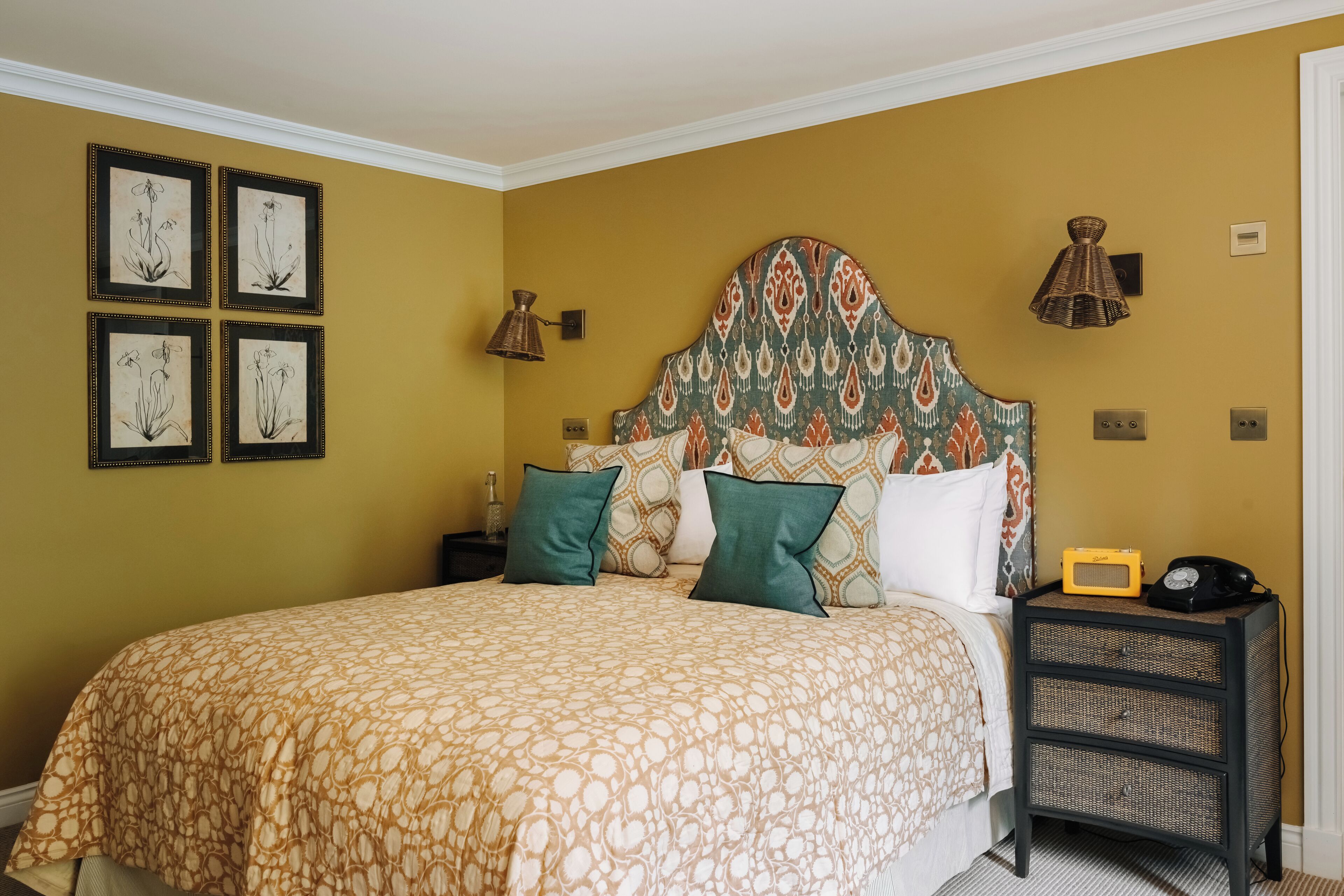 Un dormitorio con cama, lámparas de noche, mesita de noche y cuadros en la pared.
