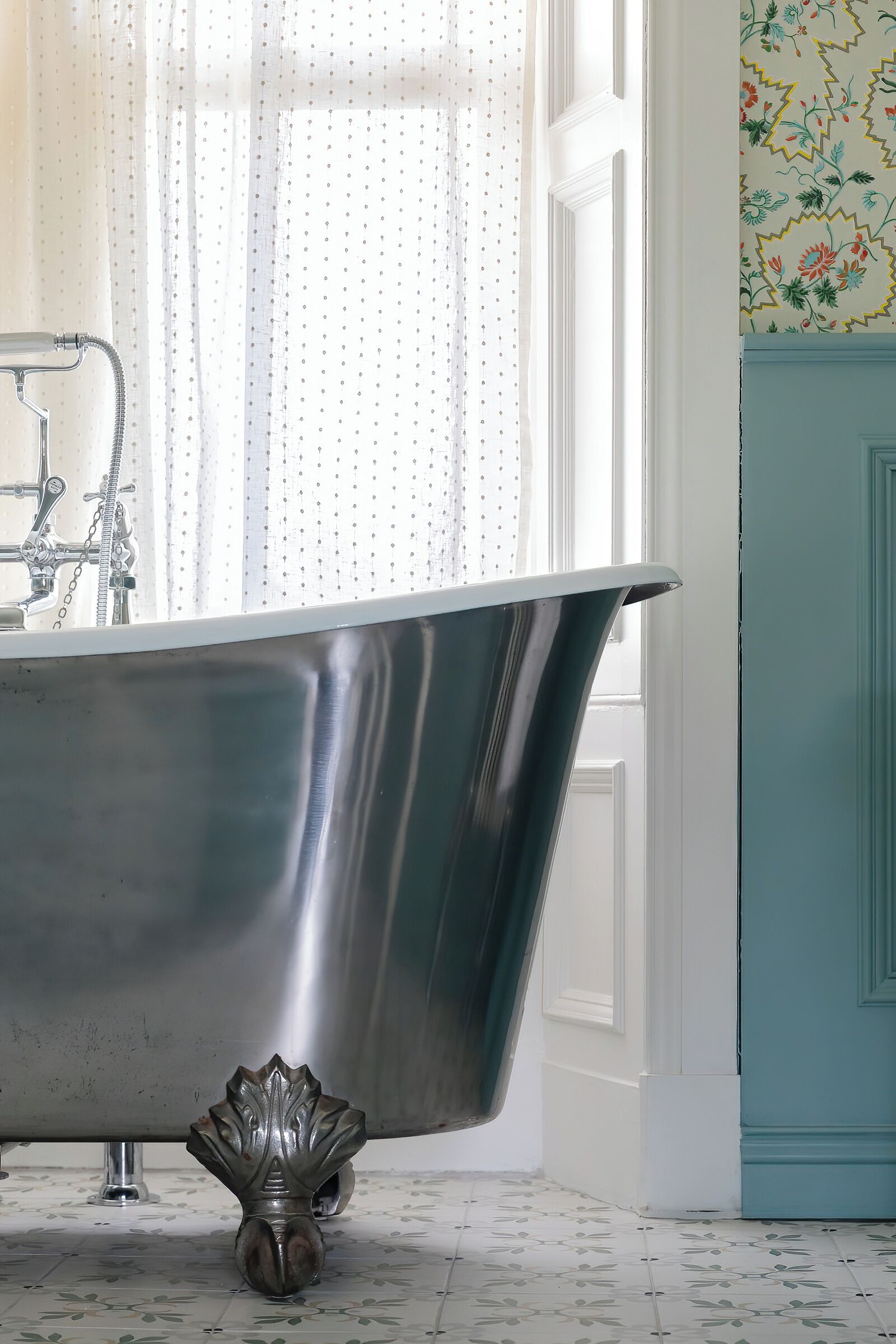 A bathroom with a freestanding bathtub, a window with sheer curtains, and a patterned wall.